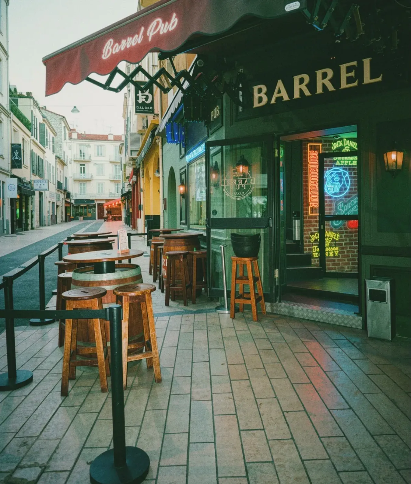 La rue piétonne devant le Barrel Pub en plein jour : les tonneaux et les tabourets alignés sous l'auvent, la rue vide