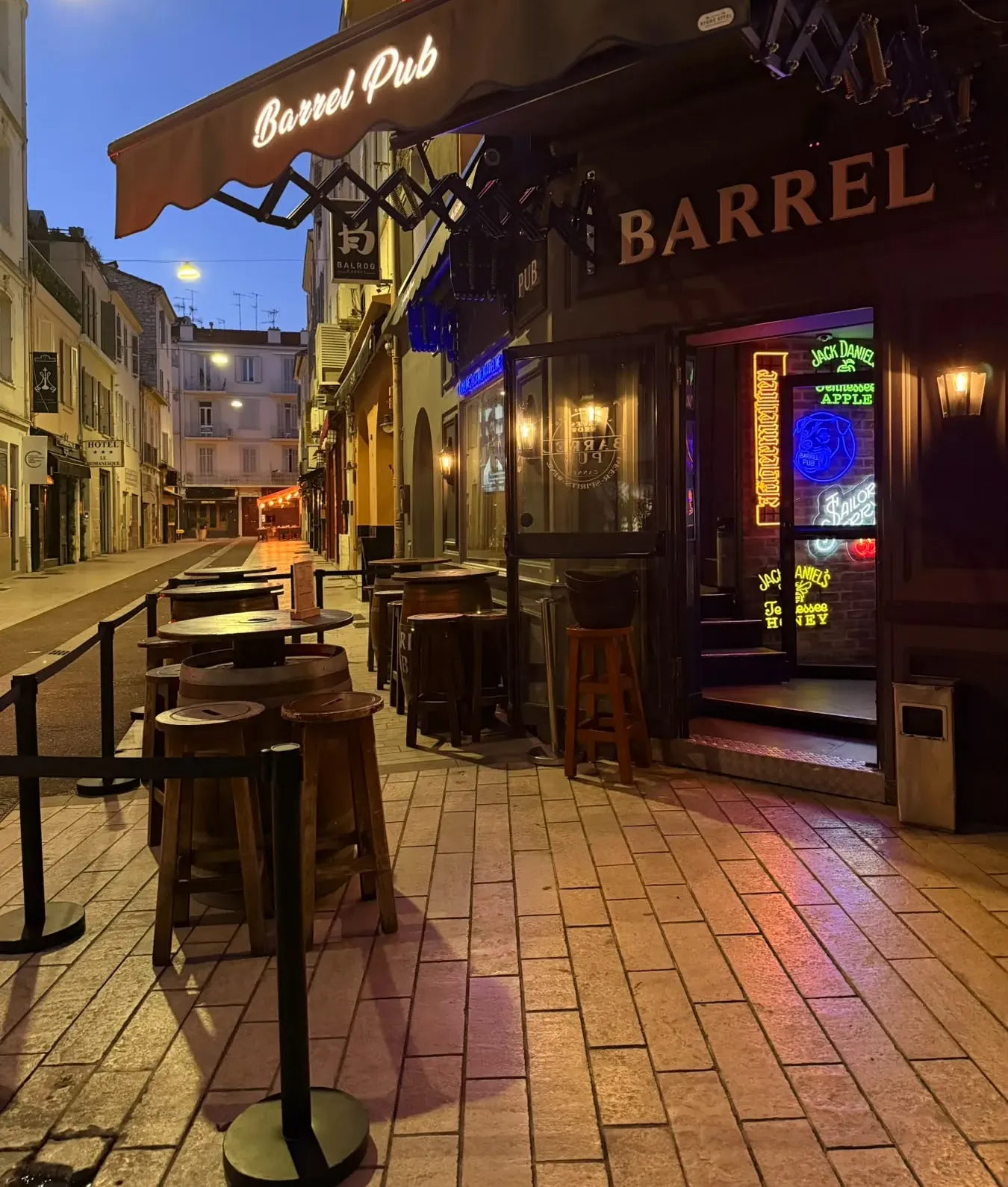 La même rue à la nuit tombée : l'enseigne Barrel et les néons de la porte allumés